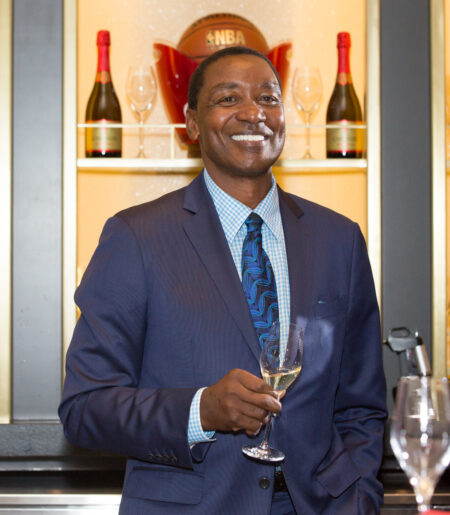 Isiah Thomas, star du basket-ball du Temple de la renommée de la NBA, dévoile son champagne Cheurlin de luxe Isiah Thomas smiles while holding a glass of champagne, with wine glasses and champagne bottles displayed in the background.