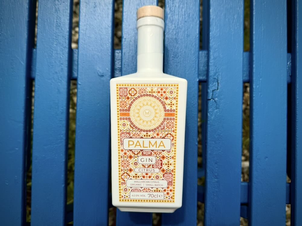 Bouteille de gin Palma avec une étiquette colorée aux motifs d'agrumes, posée sur une surface en bois bleu.