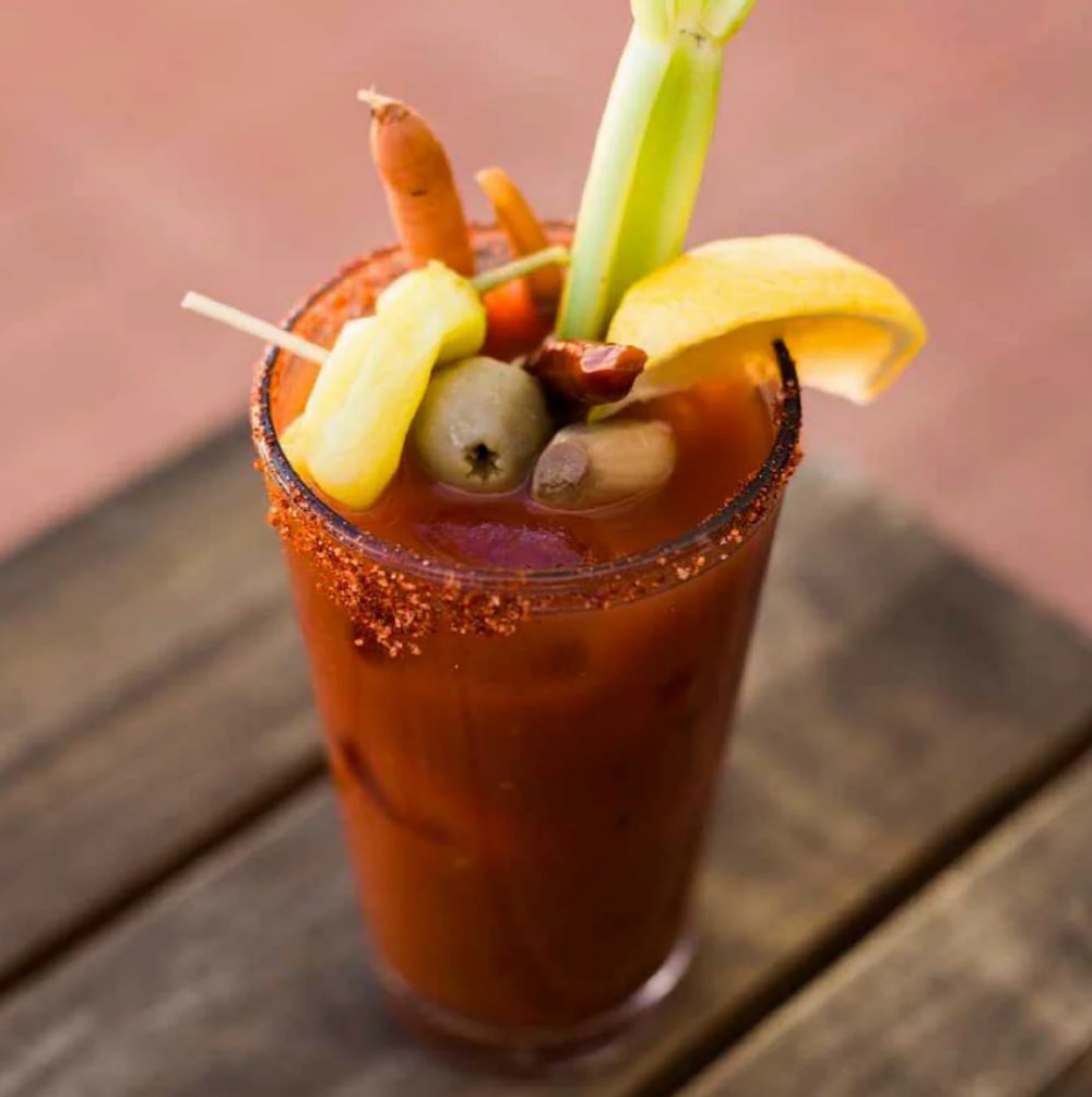 Bloody Mary garni de céleri, d'olives, de citron et de légumes marinés dans un verre sur une table en bois.