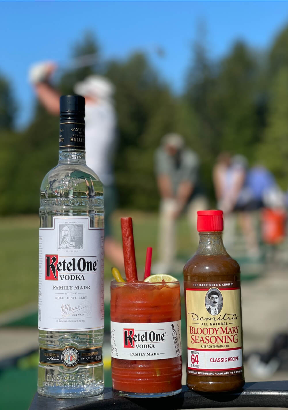 Ketel Une bouteille de vodka, un Bloody Mary garni de céleri et de citron et l'assaisonnement Bloody Mary de Demitri sur un terrain de golf.
