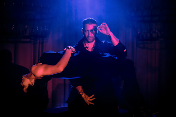 Un magicien réalise une illusion avec une femme en lévitation sur une scène sous un éclairage bleu spectaculaire au Salvage City Supper Club.