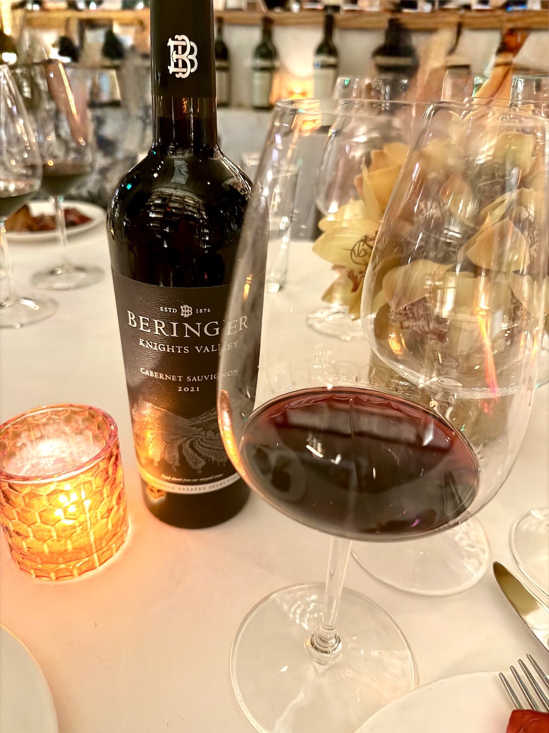 Bouteille Beringer Knights Valley Cabernet Sauvignon 2021 à côté d'un verre de vin rempli et d'une bougie allumée sur une table à manger.