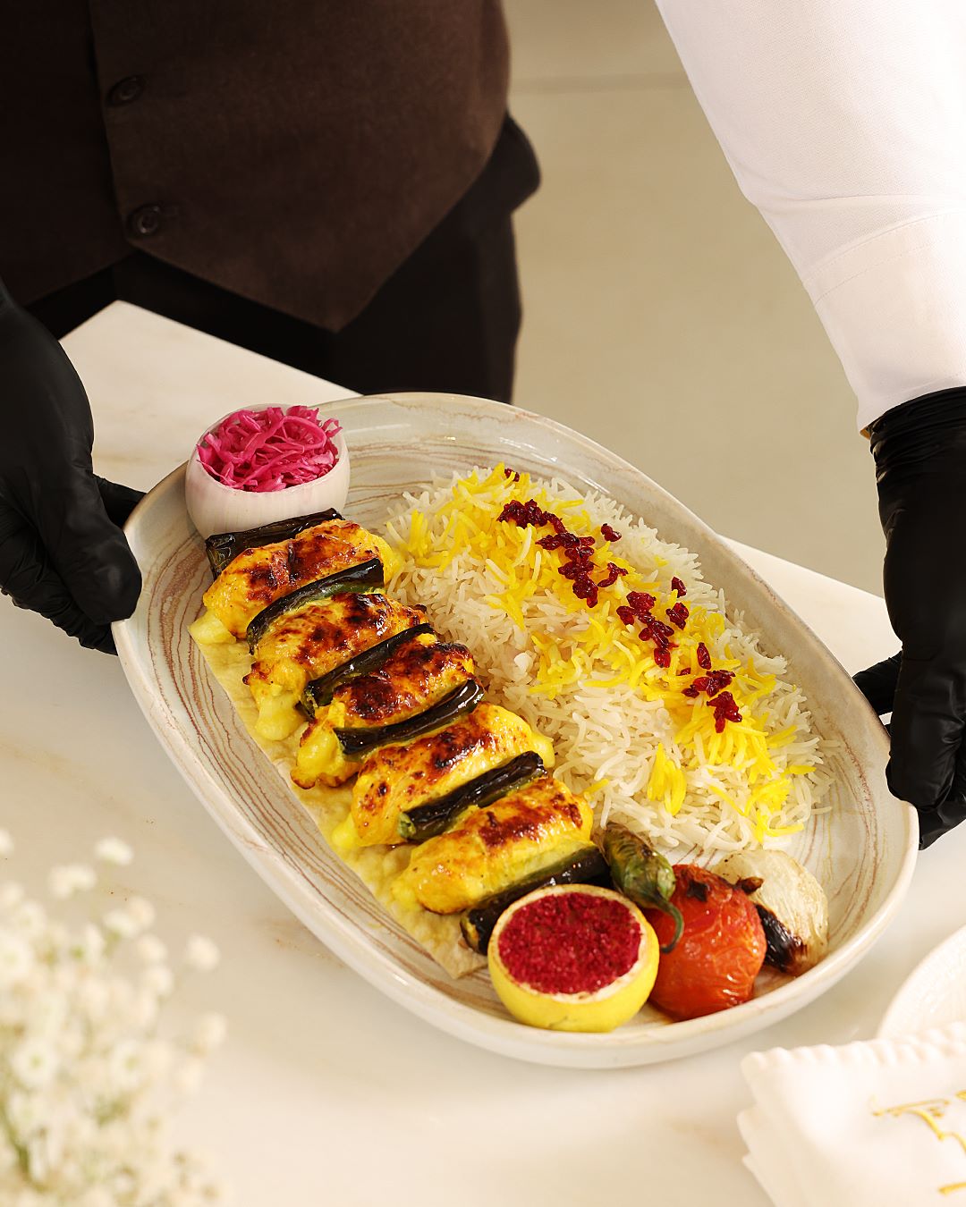 Brochettes persanes grillées servies avec du riz au safran, du citron, des oignons marinés et des garnitures sur une grande assiette ovale.