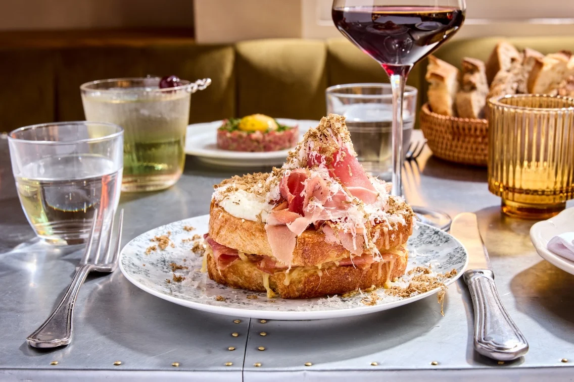 Un croque monsieur joliment plaqué avec des couches de jambon et de fromage, entouré de verres d'eau et de vin sur une table à manger.