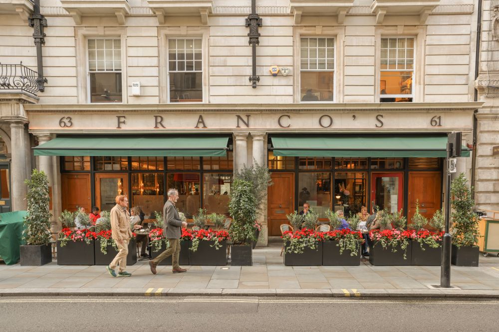 Extérieur du restaurant Franco à Mayfair, avec terrasse ornée de fleurs aux couleurs vives dans une rue animée.