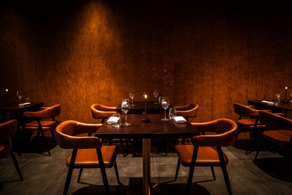 Salle à manger élégante avec des murs en bois sombre, des chaises confortables et des tables éclairées aux chandelles, créant une atmosphère intime pour les repas.