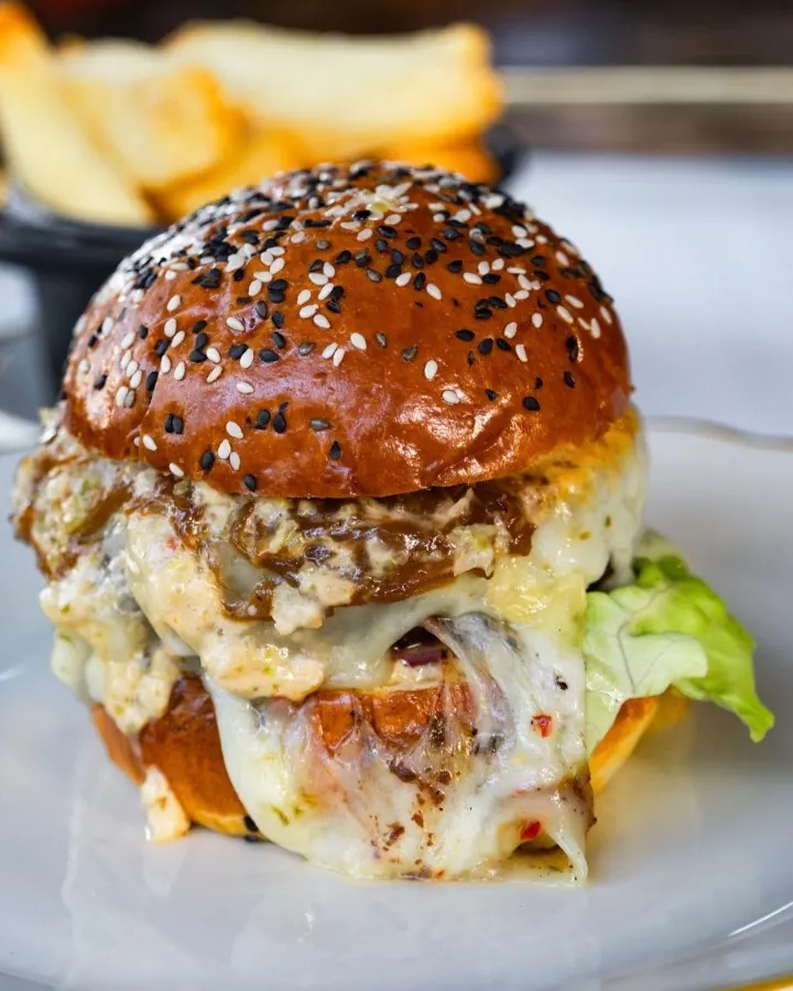 Un burger gastronomique avec du fromage fondu, des garnitures étagées et un petit pain aux graines de sésame, servi avec des frites croustillantes.