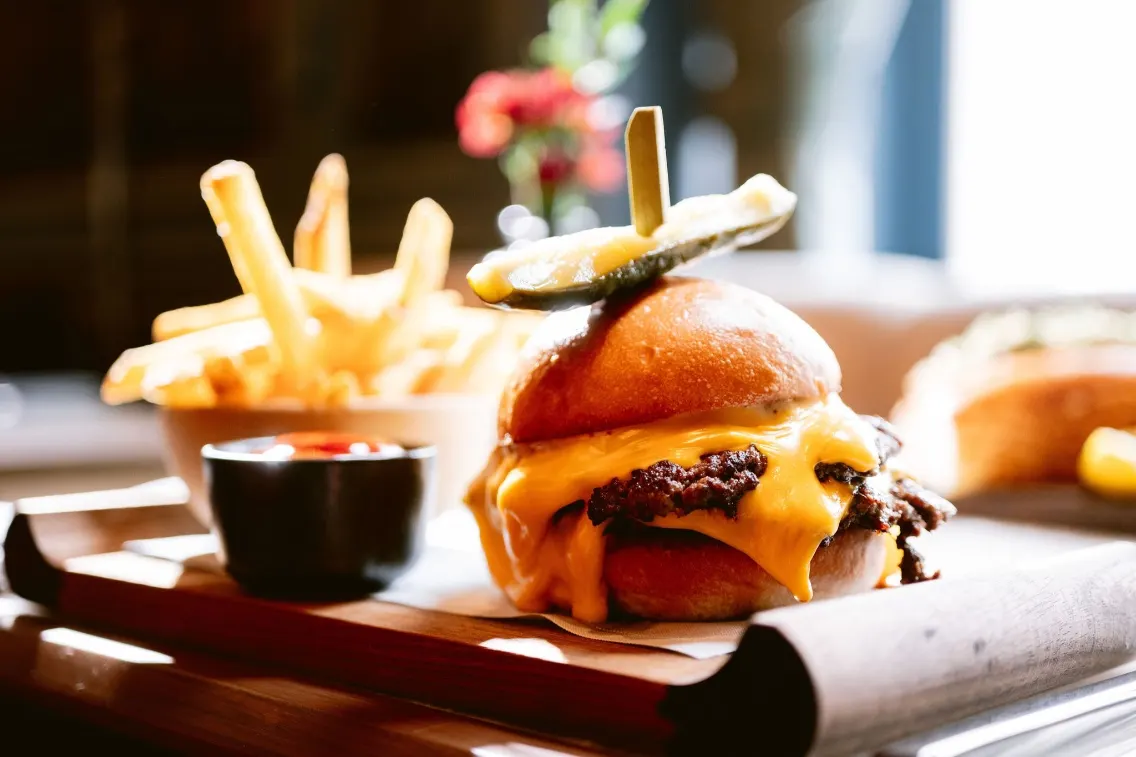 Un cheeseburger gastronomique avec du fromage fondu, des cornichons et des frites servi avec une trempette, présenté au Bruma au Ritz-Carlton.